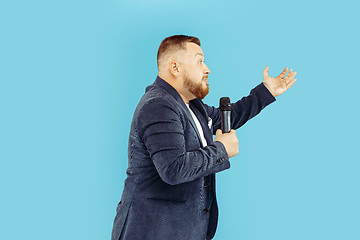 Image showing Young man with microphone on blue background, leading concept