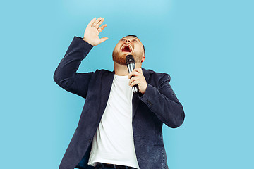 Image showing Young man with microphone on blue background, leading concept