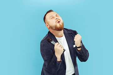 Image showing Young man with microphone on blue background, leading concept