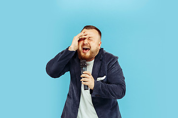 Image showing Young man with microphone on blue background, leading concept