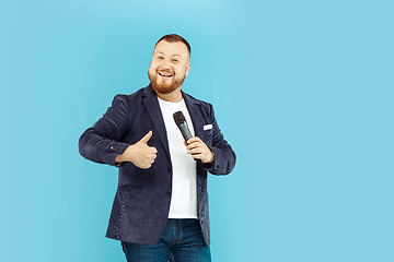 Image showing Young man with microphone on blue background, leading concept