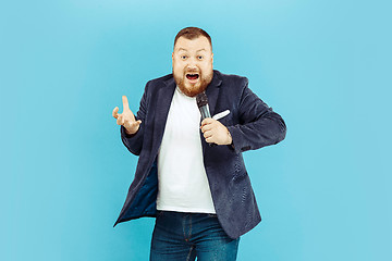 Image showing Young man with microphone on blue background, leading concept