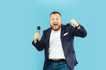 Image showing Young man with microphone on blue background, leading concept