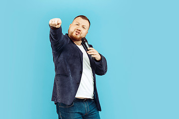 Image showing Young man with microphone on blue background, leading concept