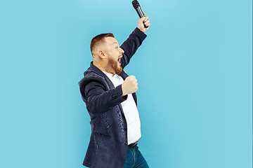 Image showing Young man with microphone on blue background, leading concept