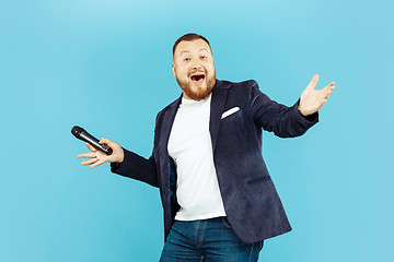 Image showing Young man with microphone on blue background, leading concept