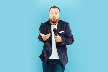 Image showing Young man with microphone on blue background, leading concept