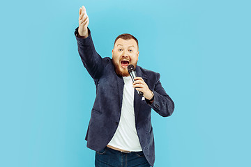 Image showing Young man with microphone on blue background, leading concept