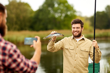 Image showing friend photographing fisherman with fish at lake