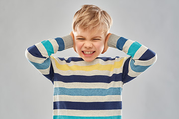 Image showing stressed boy in pullover closing ears by hands