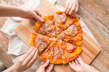 Image showing close up of hands sharing pizza on wooden table