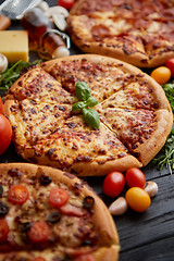 Image showing Freshly served, three various pizzas placed among tasty ingredients. Top view