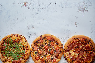 Image showing Three different kind of pizzas placed in a row on white rusty ta