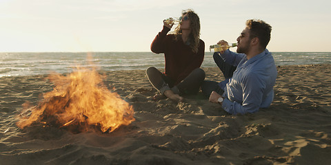 Image showing Loving Young Couple Sitting On The Beach beside Campfire drinkin