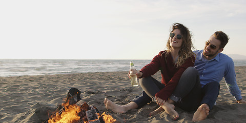 Image showing Loving Young Couple Sitting On The Beach beside Campfire drinkin