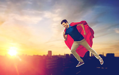 Image showing man in superhero cape flying over sunset in city