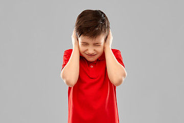 Image showing stressed boy in red t-shirt closing ears by hands