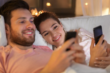 Image showing happy couple using smartphones in bed at night