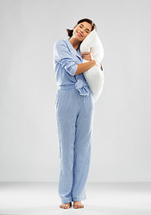 Image showing happy young woman in blue pajama hugging pillow