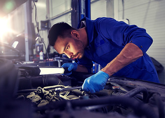 Image showing mechanic man with lamp repairing car at workshop