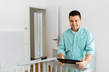 Image showing father with tablet pc assembling baby bed at home