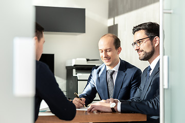 Image showing Group of confident successful business people reviewing and signing a contract to seal the deal at business meeting in modern corporate office.