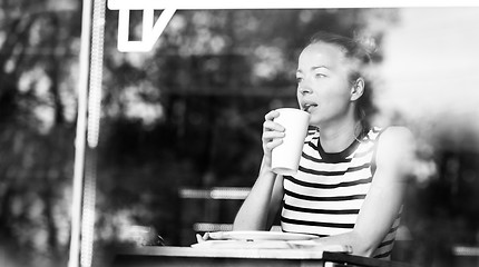 Image showing Young caucasian woman sitting alone in coffee shop thoughtfully leaning on her hand, looking trough the window