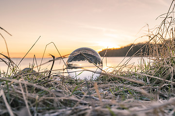 Image showing Crystal ball in frozen grass by a lake in the morning