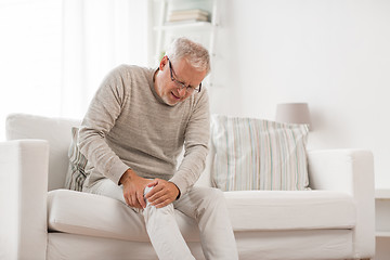 Image showing senior man suffering from knee ache at home