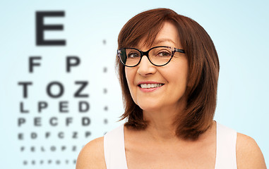 Image showing happy senior woman in glasses over eye test chart