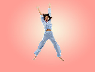 Image showing happy woman in blue pajama jumping high over pink