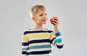 Image showing smiling boy in striped pullover eating red apple