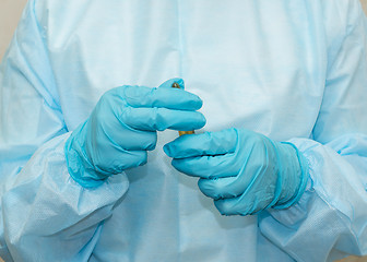 Image showing Nurse in sterile gown and gloves with an ampoule with is ready to open it
