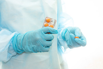 Image showing Nurse in sterile gown and gloves gives pill from pack