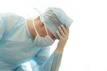 Image showing Upset surgeon in sterile gown and surgical mask props his head with hand