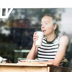 Image showing Young caucasian woman sitting alone in coffee shop thoughtfully leaning on her hand, looking trough the window