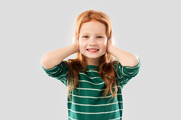 Image showing smiling red haired girl closing ears by hands