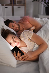 Image showing woman using smartphone while boyfriend is sleeping