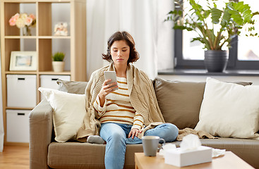 Image showing sad sick woman in blanket using smartphone at home