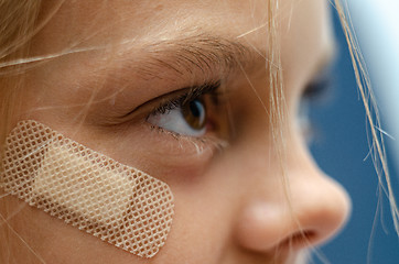 Image showing A medical band-aid is glued under the girl\'s eye