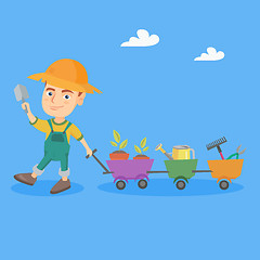 Image showing Boy pushing a cart with plants and garden tools.