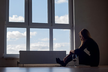 Image showing A girl with a glass of wine sits on the floor at a large stained glass window