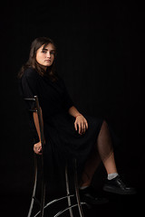 Image showing Fifteen-year-old girl sits on a bar chair, snasked on a black background in a dark