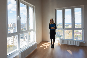 Image showing The girl with the folder stands in the middle of a large spacious room with large windows