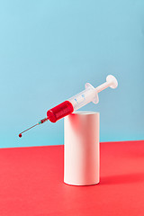 Image showing Disposable syringe with drop of red liquid on a plaster cylinder.