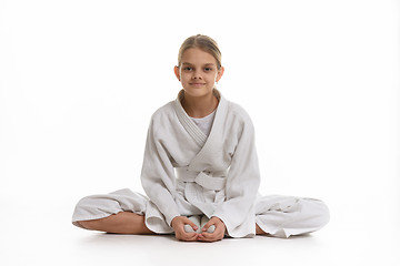 Image showing Sporting girl in keikogi sits on the floor, white background