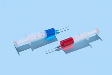 Image showing Plastic syringes of red and blue vaccine with shadows.