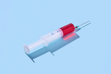 Image showing Disposable syringe of red vaccine with hard shadow.