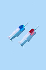 Image showing Disposable syringes of red and blue vaccine with shadows.