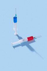 Image showing Disposable syringes of red and blue vaccine with shadows.